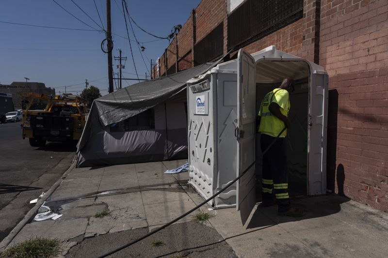 Service technician Jai Davis cleans a public bathroom across the street from Wesley Health Centers' mobile clinic in the Skid Row area of Los Angeles, Tuesday, Aug. 27, 2024. (AP Photo/Jae C. Hong)