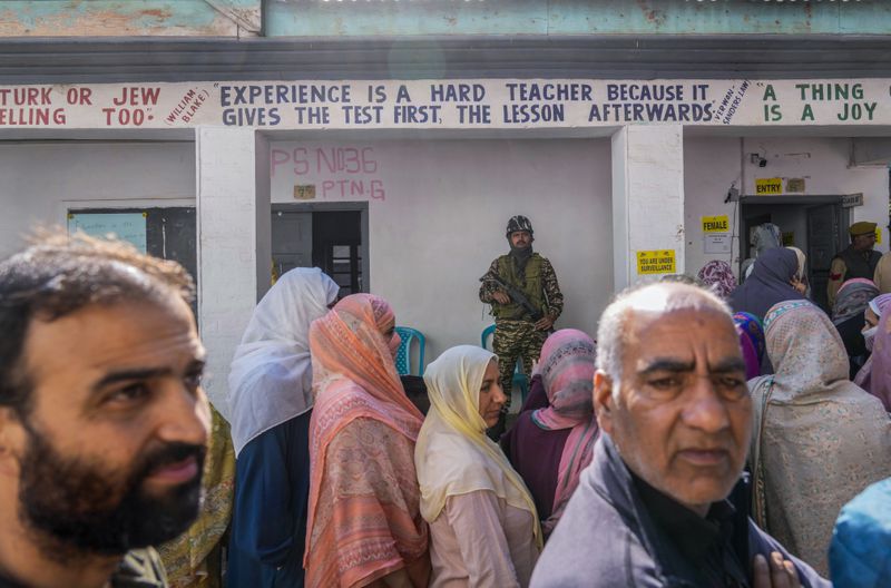 An Indian paramilitary soldier guards as Kashmiris queue up at a polling booth to cast their vote during the final phase of an election to choose a local government in Indian-controlled Kashmir, north of Srinagar, Tuesday, Oct.1, 2024. (AP Photo/Mukhtar Khan)