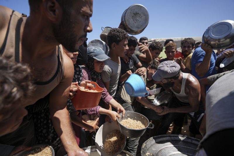 Displaced Palestinians gather for food distribution in Deir al Balah, central Gaza Strip, Friday, Aug. 23, 2024. (AP Photo/Abdel Kareem Hana)