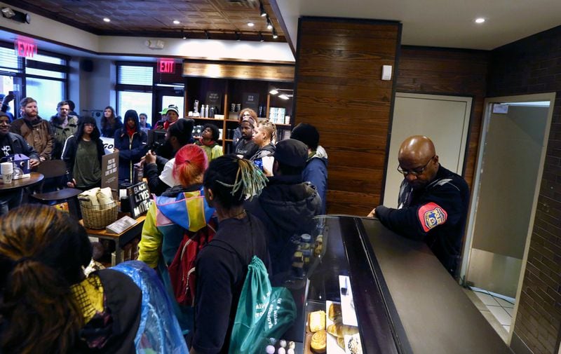 A plain-clothed police officer, right, mans a position behind the counter at the Starbucks that has become the center of protests Monday, April 16, 2018, in Philadelphia. Starbucks wants to add training for store managers on "unconscious bias," CEO Kevin Johnson said Monday, as activists held more protests at a Philadelphia store where two black men were arrested after employees said they were trespassing. (AP Photo/Jacqueline Larma)