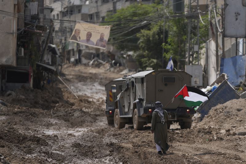 A man waves a Palestinian flag as he walks past an Israeli armored vehicle during a military operation in the West Bank refugee camp of Tulkarem, in Tulkarem Wednesday, Sept. 4, 2024. (AP Photo/ Nasser Nasser)