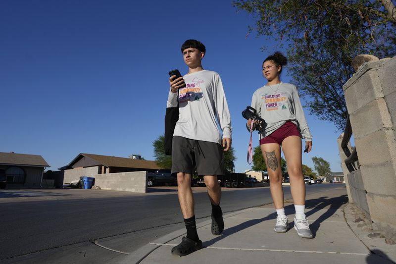 Poder In Action canvassers Lesley Chavez, left, and Andrew Chavez go door-to-door during a neighborhood voter canvassing outreach Tuesday, Sept. 3, 2024, in Phoenix. (AP Photo/Ross D. Franklin)