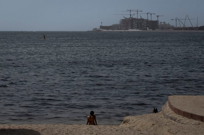 A woman sits on Dubai Marina beach, United Arab Emirates, Tuesday, Aug. 13, 2024. (AP Photo/Altaf Qadri)