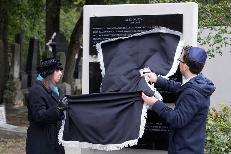 Yuval Danzig, right, the son of a Polish-Israeli man kidnapped and killed by Hamas, helps to unveil a plaque honoring his father, Alex Dancyg, in the Jewish cemetery in Warsaw, Poland, on Monday, Oct. 7, 2024. (AP Photo/Czarek Sokolowski)