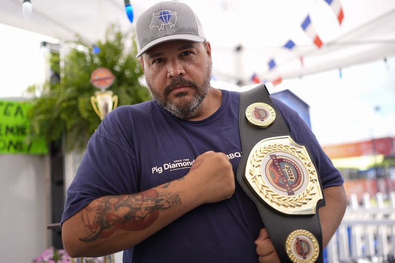 Hugo Costa from Brazil of the Pig Diamonds BBQ Team holds a belt he won in the mustard sauce competition at the World Championship Barbecue Cooking Contest, Friday, May 17, 2024, in Memphis, Tenn. (AP Photo/George Walker IV)