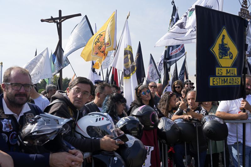 Motorcyclists holding their helmets and their groups' banners gather at the Roman Catholic holy shrine of Fatima to attend the IX Pilgrimage of the Blessing of Helmets that draws tens of thousands, in Fatima, Portugal, Sunday, Sept. 22, 2024. (AP Photo/Ana Brigida)