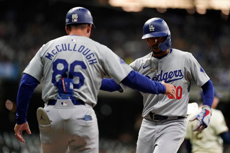 Los Angeles Dodgers' Mookie Betts, right, is congratulated by first base coach Clayton McCullough, left, after hitting an RBI single during the seventh inning of a baseball game against the Milwaukee Brewers, Monday, Aug. 12, 2024, in Milwaukee. (AP Photo/Aaron Gash)