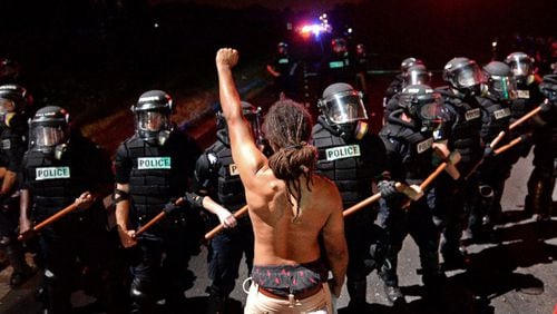 A protester stands with his left arm extended and fist clenched in front of a line of police officers holding batons in Charlotte, North Carolina, Sept. 20, 2016.