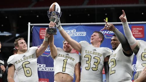 Calhoun's Bailey Lester (6), Porter Law (1), Zeke Nance (33) and C.J. Fuller (52) celebrate with the trophy after their win against Peach County during the Class AAA Championship at Mercedes-Benz Stadium Friday, December 8, 2017, in Atlanta. Calhoun won 10-6. PHOTO / JASON GETZ