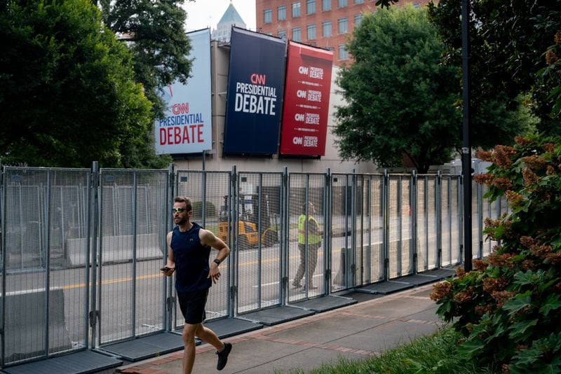 A man runs along 10th street as workers assemble security fencing on Thursday, June 27, 2024 (Ben Hendren for the Atlanta Journal-Constitution)