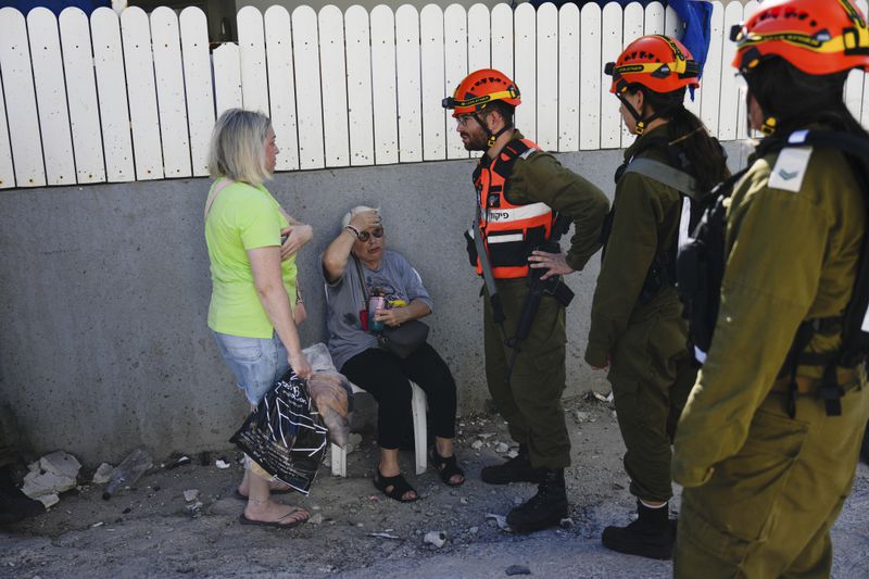 Israeli soldiers from the Homefront Command unit treat an elderly woman at the site that was hit by a rocket fired from Lebanon, in Kiryat Yam, northern Israel, on Tuesday, Oct. 8, 2024. (AP Photo/Ariel Schalit)