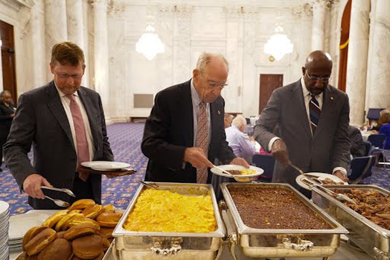 (Left to right): John Isakson, son of late U.S. Sen. Johnny Isakson, and Sens. Chuck Grassley of Iowa and Raphael Warnock of Georgia load up their plates during the annual bipartisan Senate luncheon on Thursday.