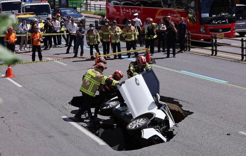 South Korean firefighters check a vehicle that fell into a sinkhole on a street in Seoul, South Korea, Thursday, Aug. 29, 2024. (Seo Dae-yeon/Yonhap via AP)