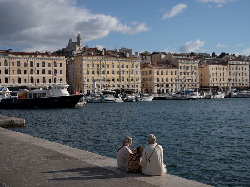 Women sit along the Vieux Port in Marseille, southern France, Monday, April 22, 2024. (AP Photo/Daniel Cole)