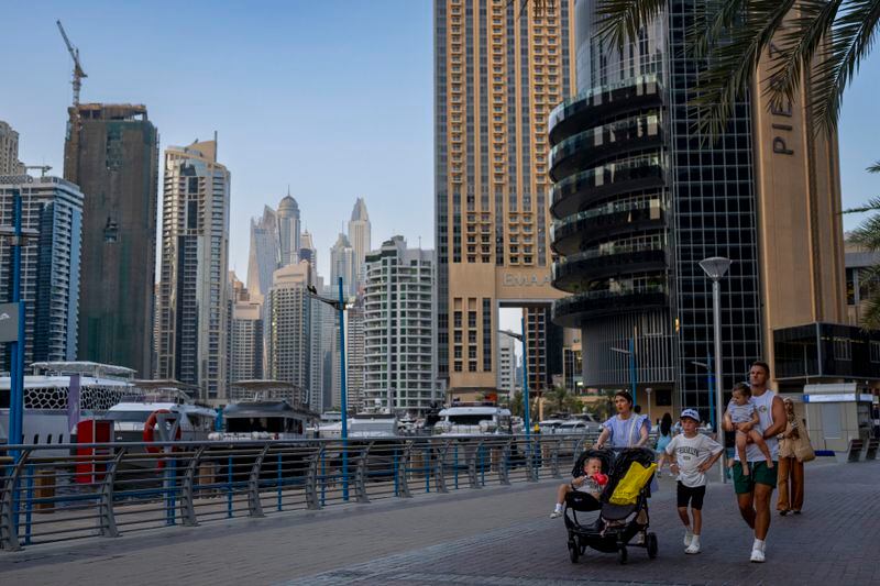 A family takes a walk along Dubai Marina Walk in Dubai, United Arab Emirates, Tuesday, Aug. 13, 2024. (AP Photo/Altaf Qadri)