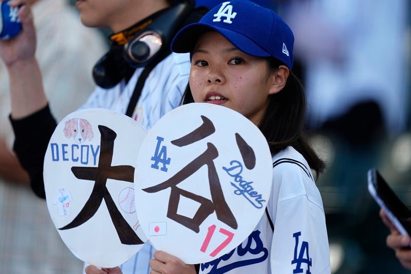 A Los Angeles Dodgers fan holds up signs for Shohei Ohtani who warms up before a baseball game against the Colorado Rockies, Saturday, Sept. 28, 2024, in Denver. (AP Photo/David Zalubowski)