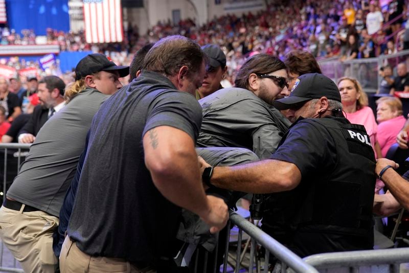 Police remove a man, center with sunglasses, who had climbed onto the media riser, as Republican presidential nominee former President Donald Trump speaks at a campaign event, Friday, Aug. 30, 2024, in Johnstown, Pa. (AP Photo/Alex Brandon)