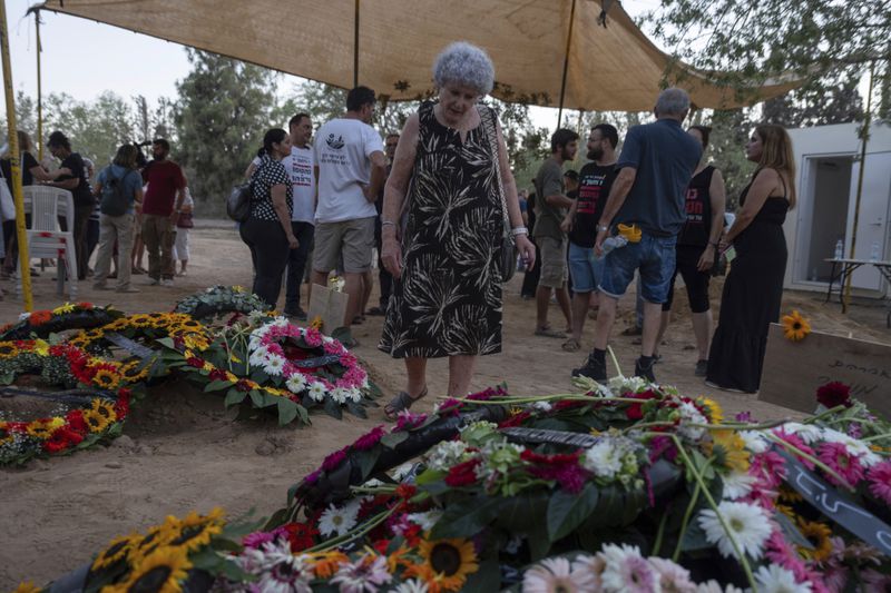 Widow Ruti Munder stands near the grave of her husband Avraham Munder, who was killed in Hamas captivity in the Gaza Strip and recovered by the Israeli military in Gaza, at Kibbutz Nir Oz, southern Israel, Wednesday, Aug. 21, 2024. Their son, Roee Munder, who was killed on Oct. 7, 2023, was reburied at the Kibbutz. (AP Photo/Ohad Zwigenberg)