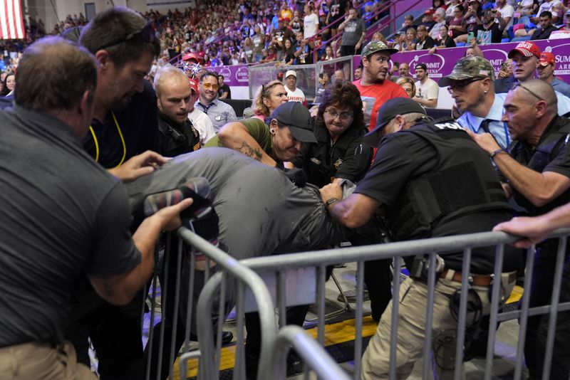 Police remove a man, center, who had climbed over barricades and onto the media riser, as Republican presidential nominee former President Donald Trump speaks at a campaign event, Friday, Aug. 30, 2024, in Johnstown, Pa. (AP Photo/Alex Brandon)