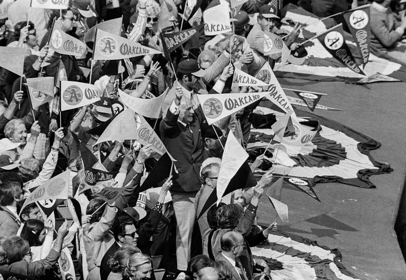 FILE - Owner Charles Finley, center, waves a pennant along with a group of fans, as they cheer on the Oakland As, after catcher Gene Tenace connected for his fourth home run of the World Series, Oct. 20, 1972, Oakland, Calif. (AP Photo)