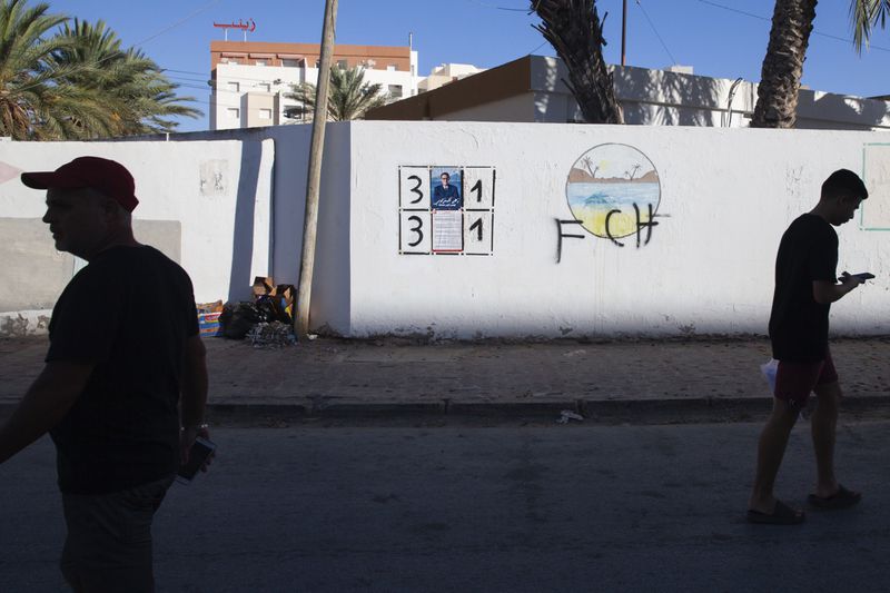 People walk past a wall with electoral banners in Sfax, Tunisia, Sunday, Sept. 15, 2024, ahead of the upcoming presidential elections. (AP Photo/Ons Abid)